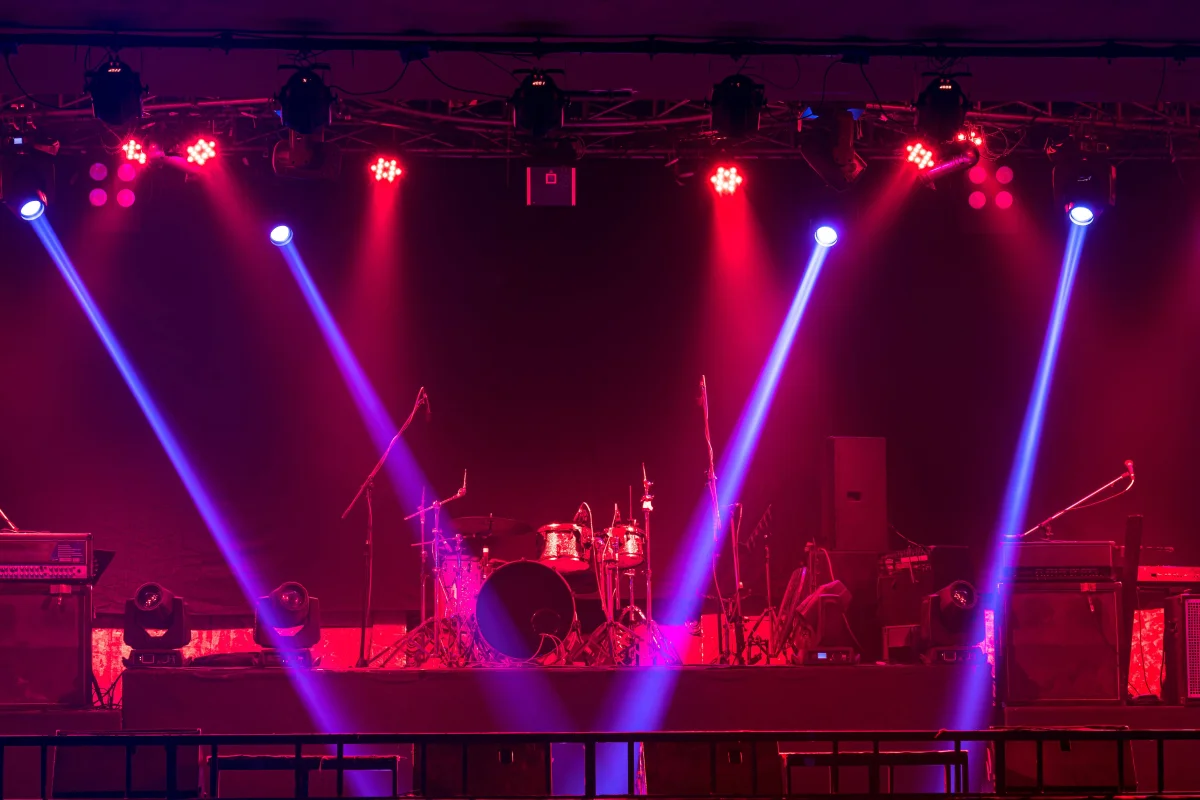 Escenario profesional con focos cruzados en rojo y azul sobre un kit de batería, ambiente de concierto en directo